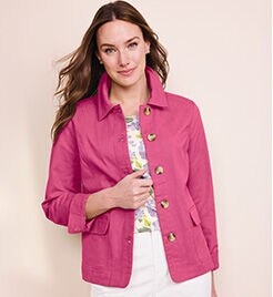 model smiling into the camera wearing a pink jacket with white, floral shirt underneath and white pants