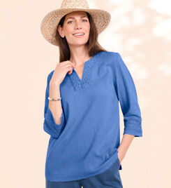 smiling model wearing a blue tops and blue pants with tan hat