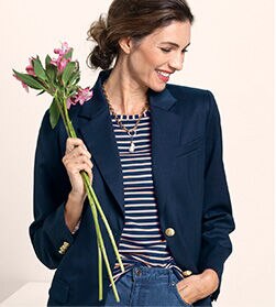model wearing a dark blazer over a striped shirt with blue jeans, holding a small bunch of flowers