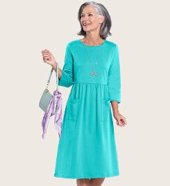 woman smiling to the left wearing a light teal dress and holding a purse with a ribbon tied to the handle