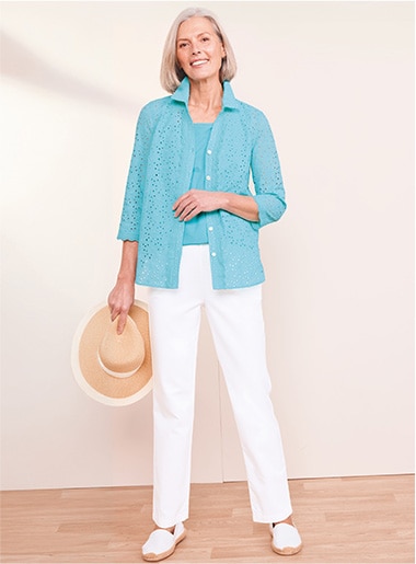 model wearing dark blue top and striped white and blue pants with white shoes, holding a tan purse and white jacket over the shoulder